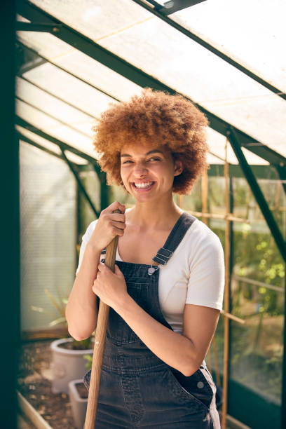 Portrait Of Smiling Woman With Broom Working In Greenhouse At Home